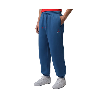 A person wearing blue sweatpants with a small red embroidered logo on the left thigh, paired with a red top and white sneakers, shown against a plain gray studio background.