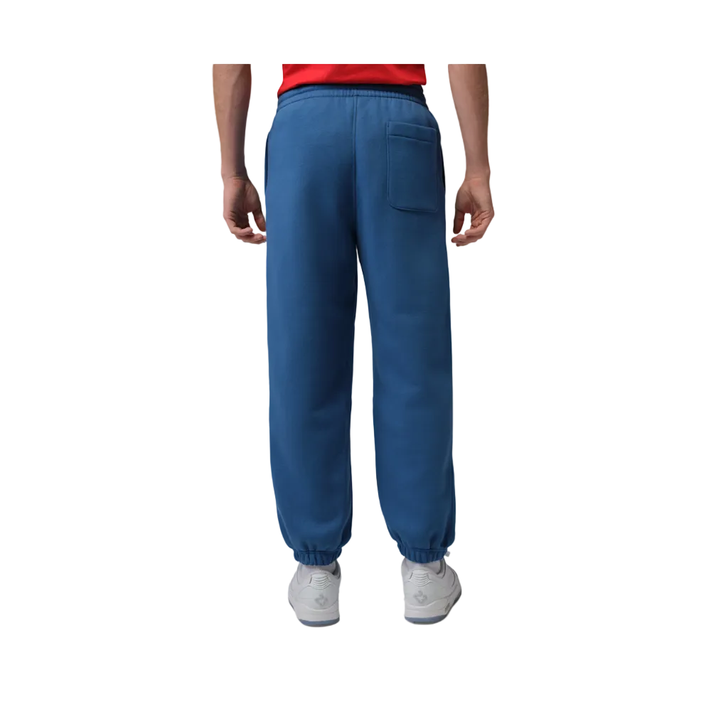 A person shown from the back wearing blue jogger-style pants with an elastic waistband, side pockets, and elastic cuffs, paired with a red top and white sneakers on a light gray studio background.