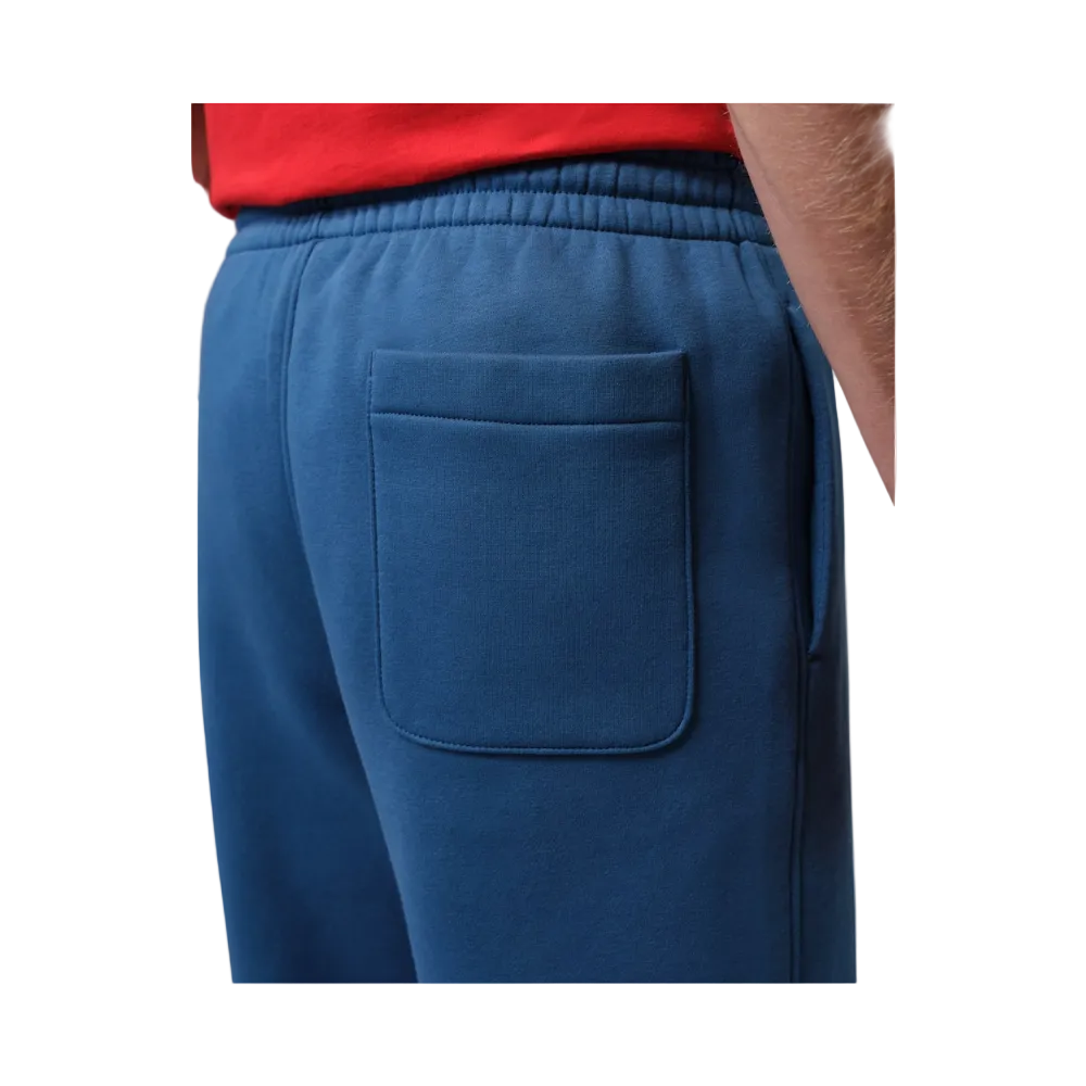 Close-up of a person wearing blue sweatpants with an elastic waistband and a large back pocket, paired with a red top. 