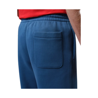 Close-up of a person wearing blue sweatpants with an elastic waistband and a large back pocket, paired with a red top. 