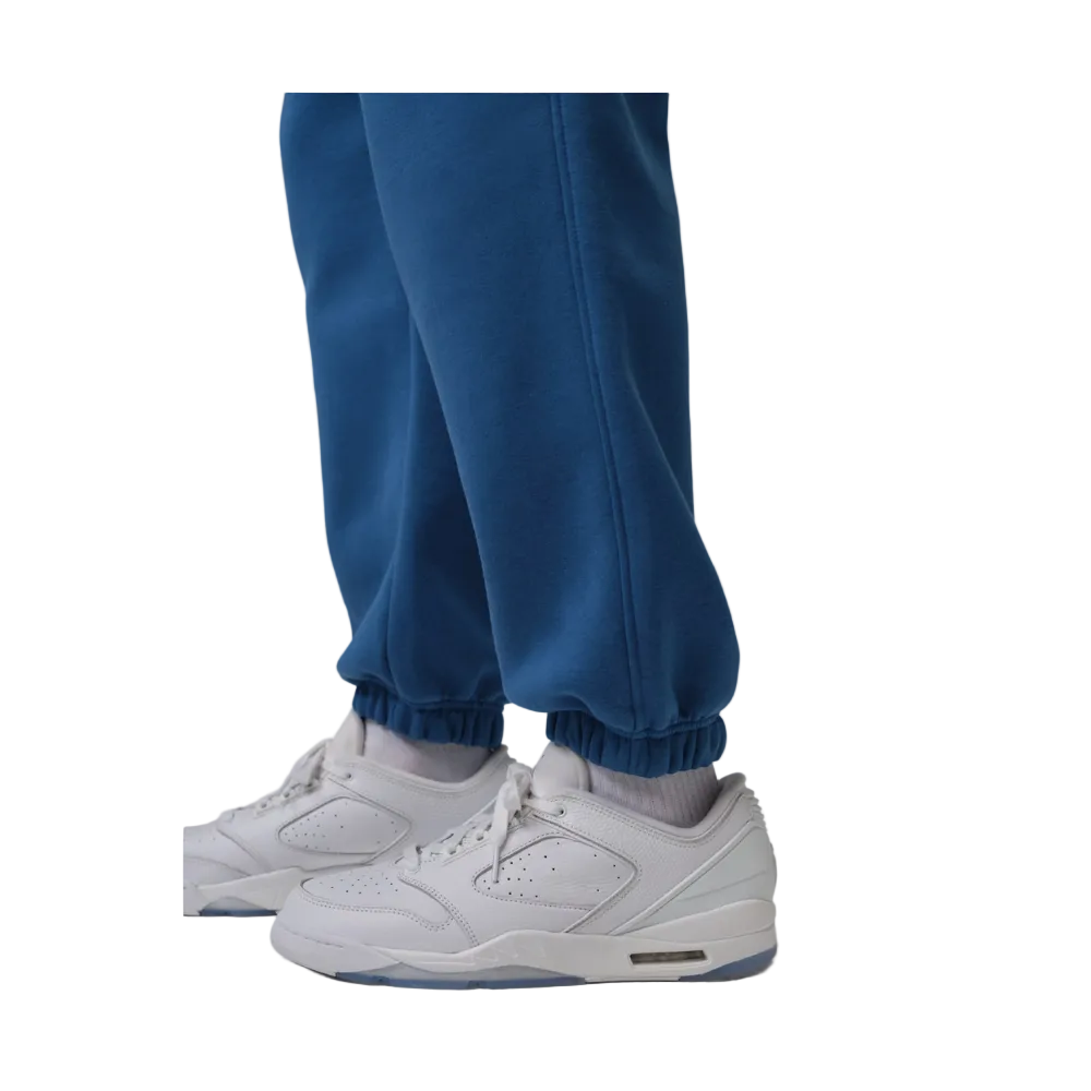 A close-up of a person's legs wearing blue jogger sweatpants and white Air Jordan 11 Retro Low sneakers with light blue accents, set against a plain gray studio background.