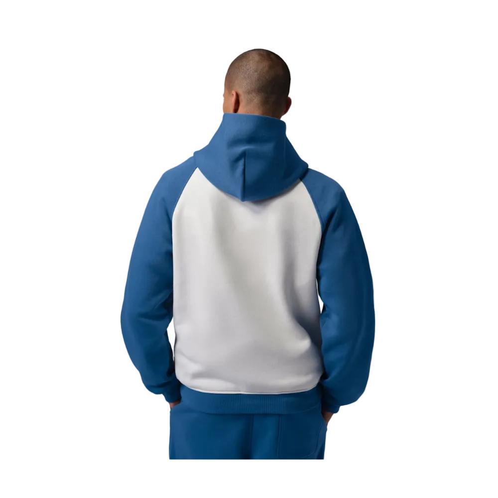 A man viewed from the back wearing a raglan-style hooded sweatshirt with a white back panel and blue sleeves and hood, paired with matching blue pants, against a plain gray studio background.