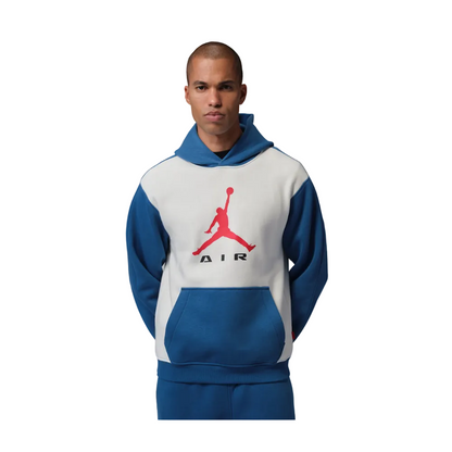 A man wearing a blue and white colorblock pullover hoodie with a red Jumpman logo on the front, paired with matching blue sweatpants, set against a solid gray studio background.