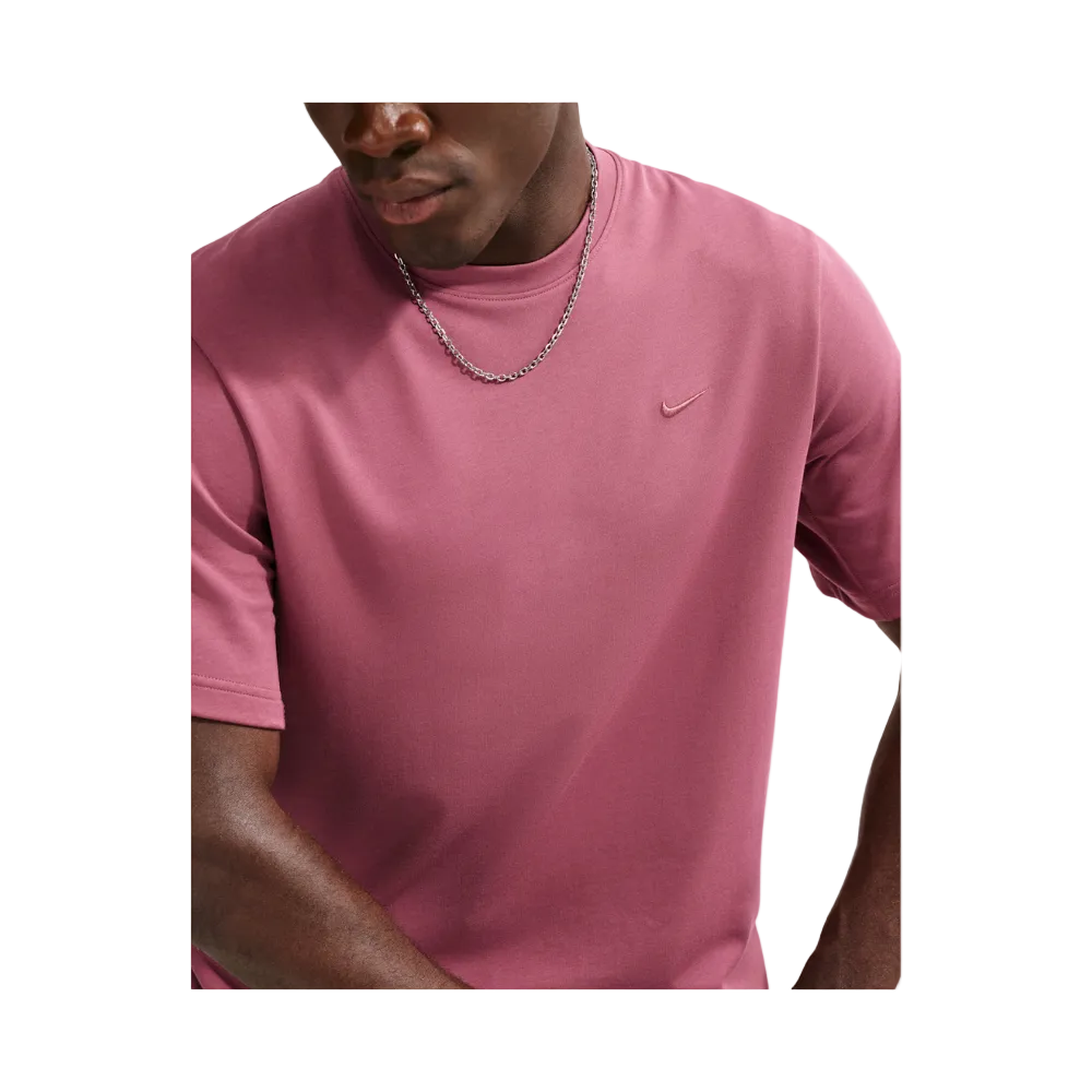 A close-up of a man wearing a dusty rose pink Nike short-sleeve t-shirt with a small tonal swoosh logo on the left chest, paired with a silver chain necklace.