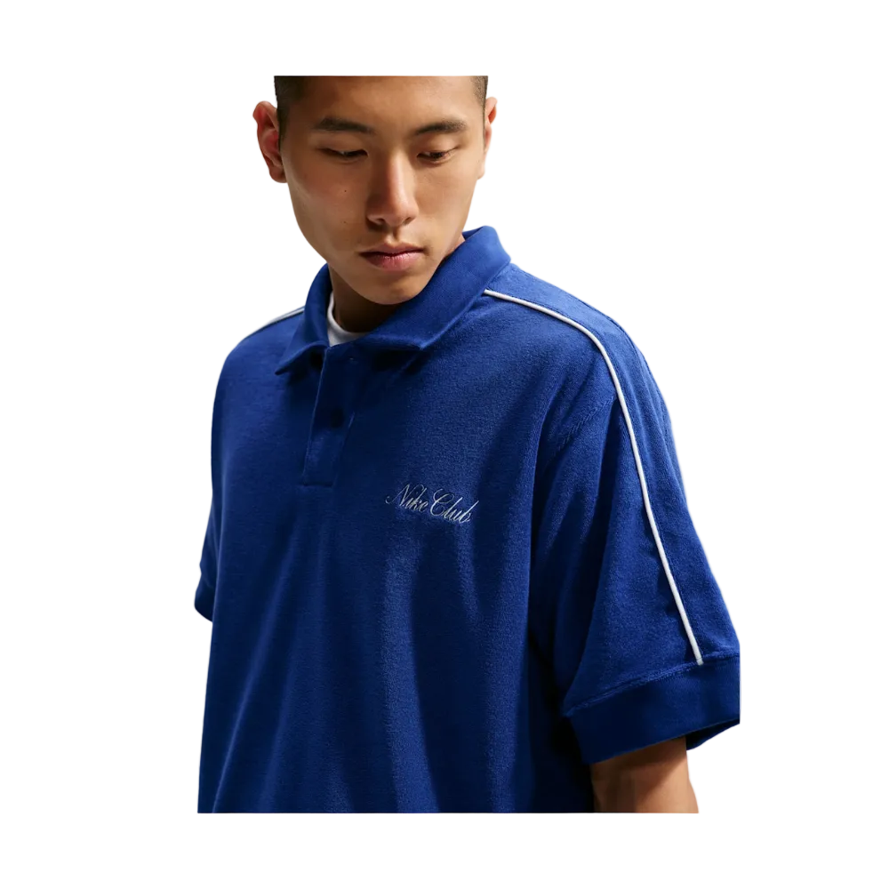 A man wearing a royal blue short-sleeve polo shirt with white piping along the shoulder and sleeve, and white script embroidery on the chest reading 'Nile Elite'.