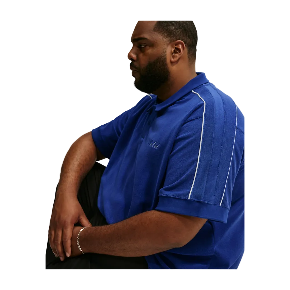 A man wearing a royal blue short-sleeve polo shirt with white piping details on the shoulders and chest, posed against a light gray background.
