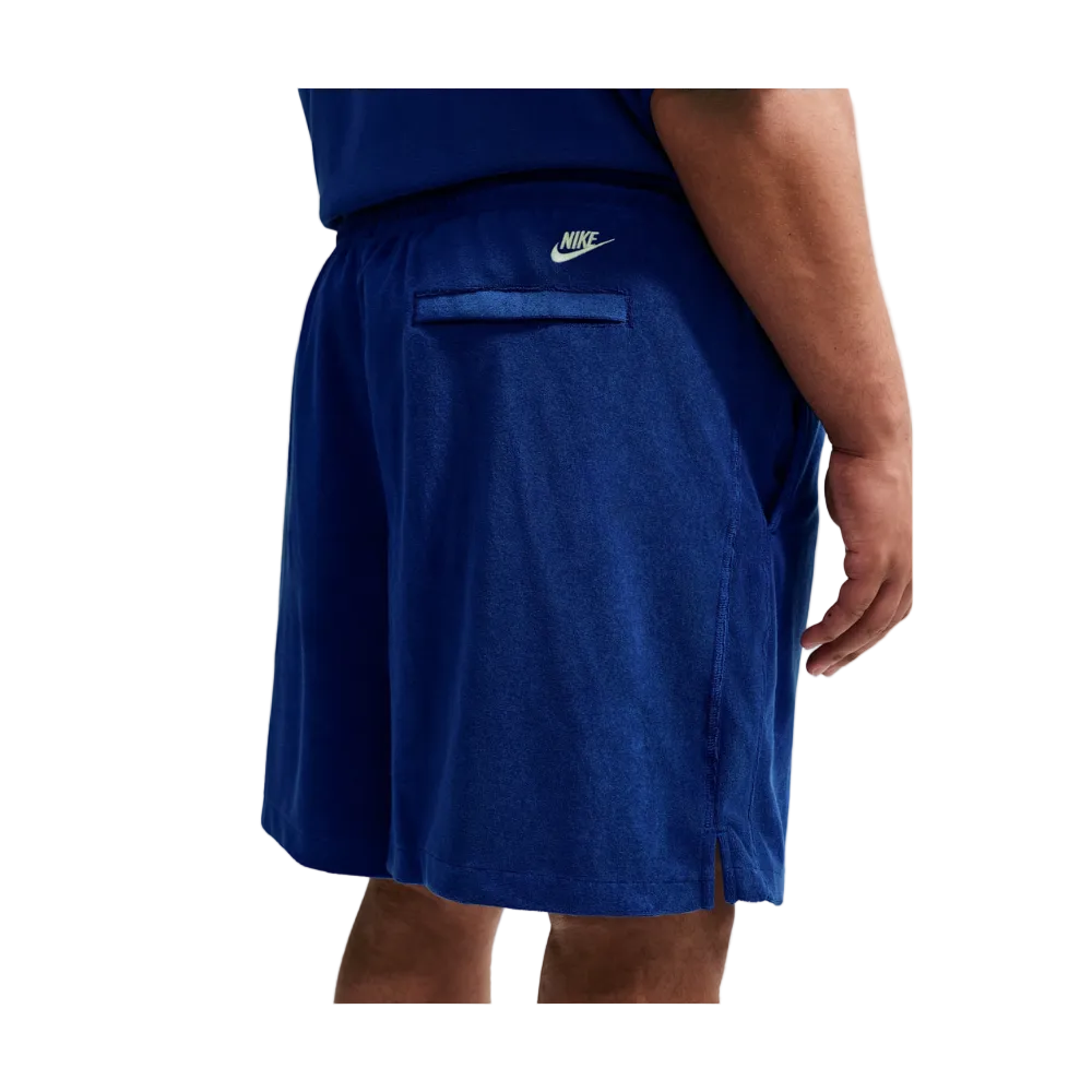 A close-up of a person wearing Nike athletic shorts in a heathered royal blue color, showing the side pocket and white Nike logo on the waistband.