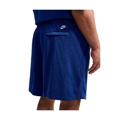 A close-up of a person wearing Nike athletic shorts in a heathered royal blue color, showing the side pocket and white Nike logo on the waistband.