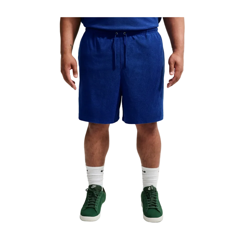 A person wearing royal blue drawstring shorts, a blue top, white socks, and green sneakers, shown from the waist down against a light gray studio background.