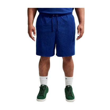 A person wearing royal blue drawstring shorts, a blue top, white socks, and green sneakers, shown from the waist down against a light gray studio background.