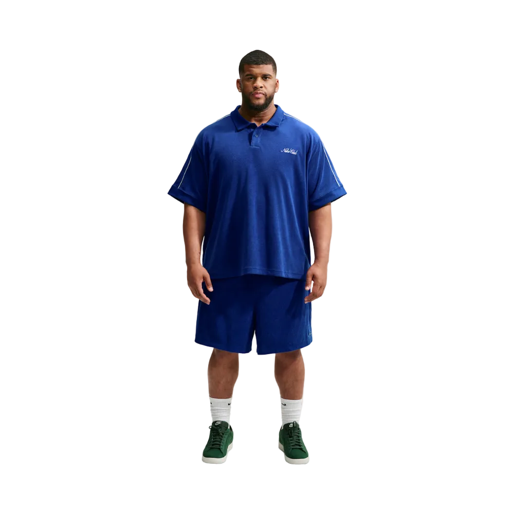 A man modeling a royal blue short-sleeve polo shirt and matching royal blue shorts against a light gray studio background.