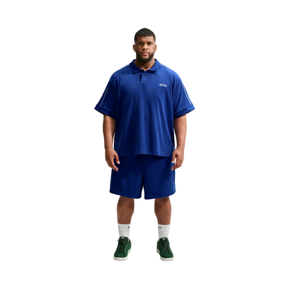 A man modeling a royal blue short-sleeve polo shirt and matching royal blue shorts against a light gray studio background.