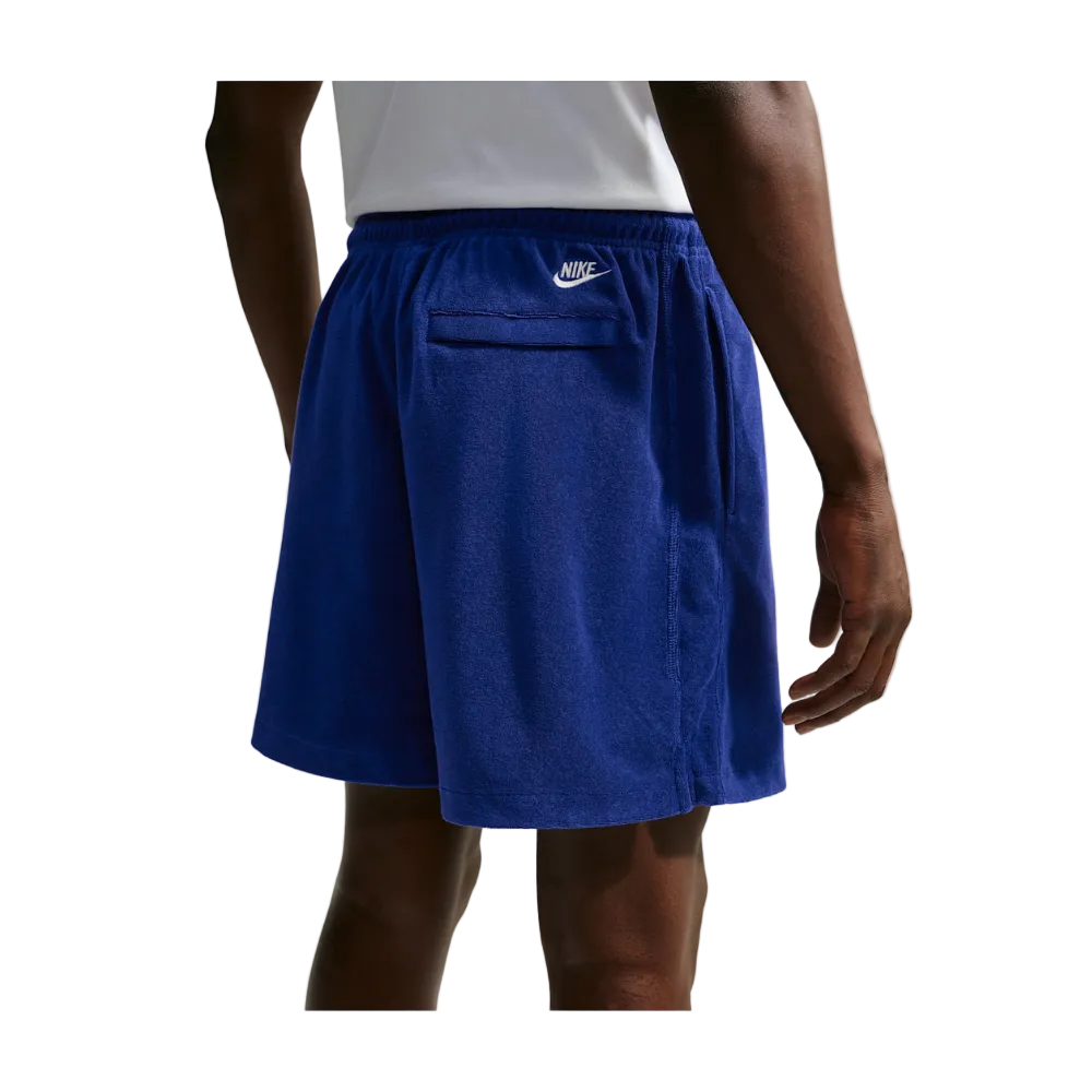 A person wearing Nike athletic shorts in a heathered royal blue color, shown from the back. The shorts feature an elastic waistband, a side pocket, and a small white Nike swoosh logo on the left side.