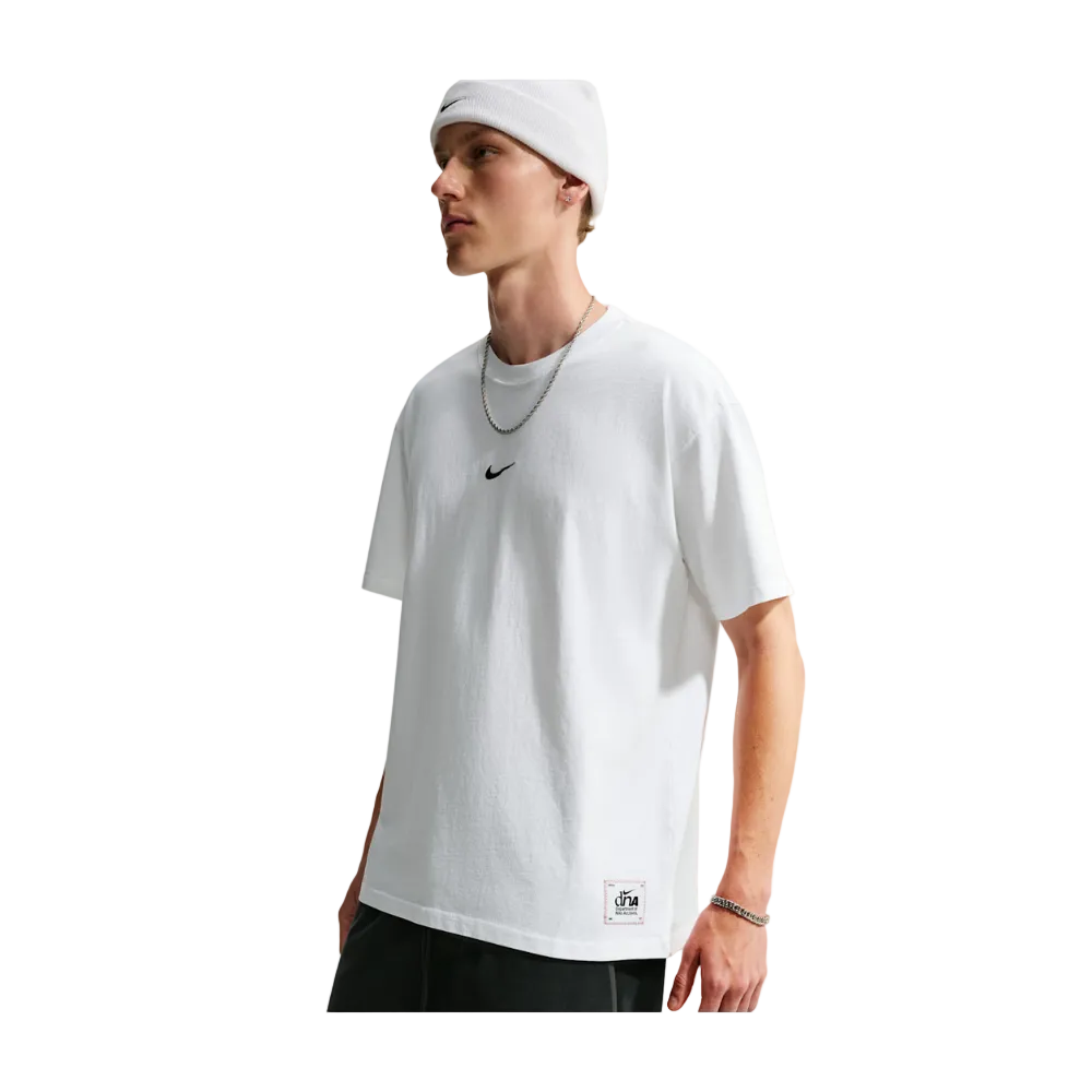 A man wearing a white short-sleeve crewneck t-shirt with a small black Nike swoosh on the chest, paired with a white beanie, silver chain necklace, and black shorts, set against a light gray studio background.