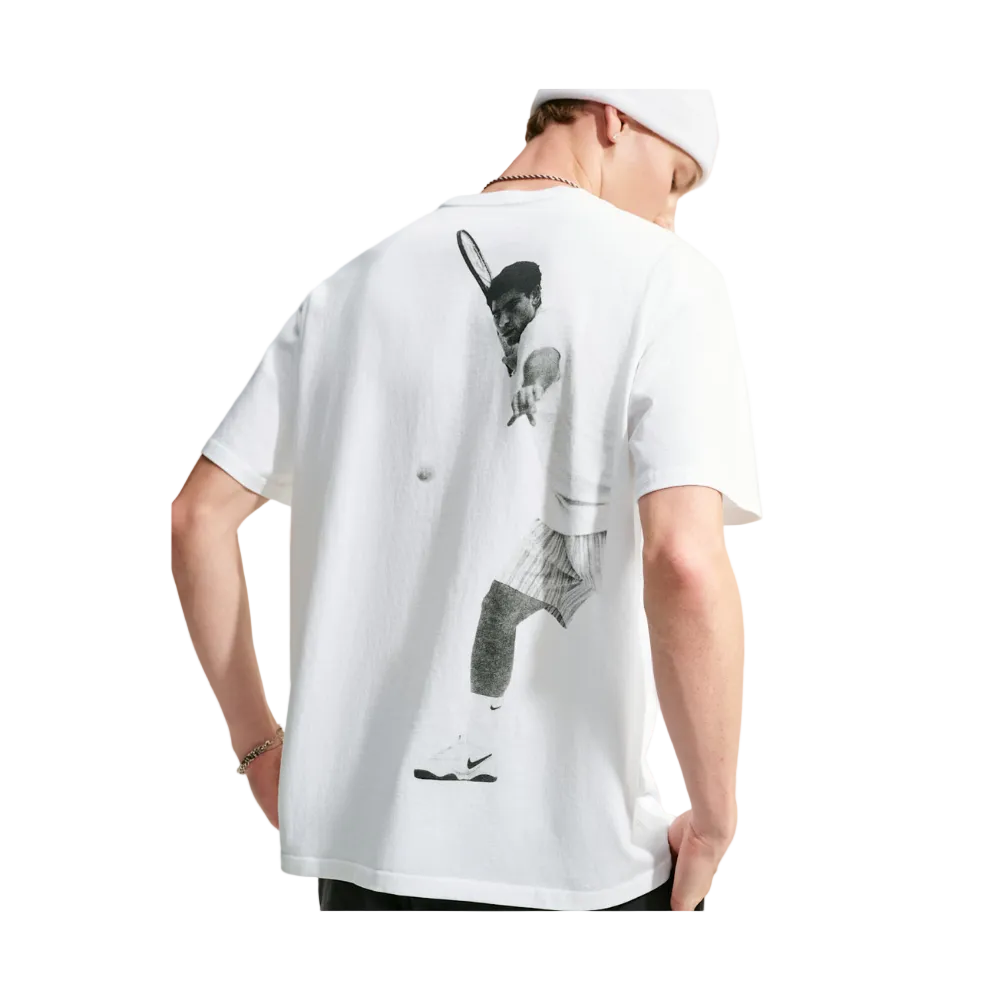 A man wearing a white t-shirt from the back, featuring a large black and white graphic print of a tennis player on the back. The man is also wearing a white cap and a necklace.