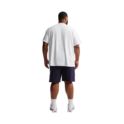 A man viewed from behind wearing an oversized white t-shirt, dark navy athletic shorts, white socks, and white sneakers, standing against a light gray studio background.