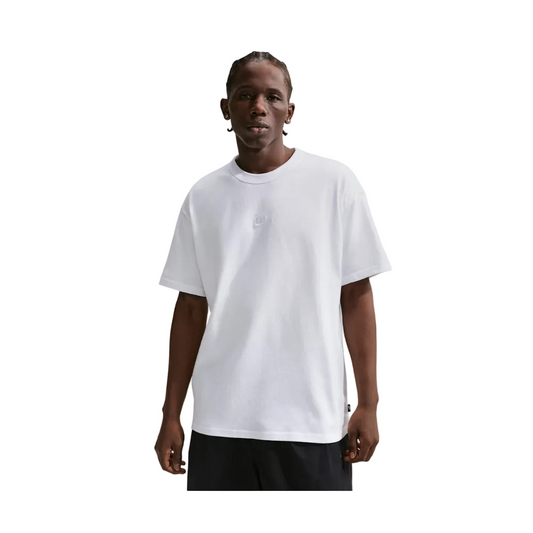 A man wearing a white short-sleeve crewneck t-shirt with a subtle tonal embroidered logo on the chest, paired with black shorts, set against a light gray studio background.