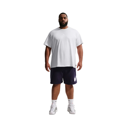 A man modeling a white Nike short-sleeve t-shirt and navy blue athletic shorts with a white Swoosh logo, paired with white socks and sneakers, against a light gray studio background.